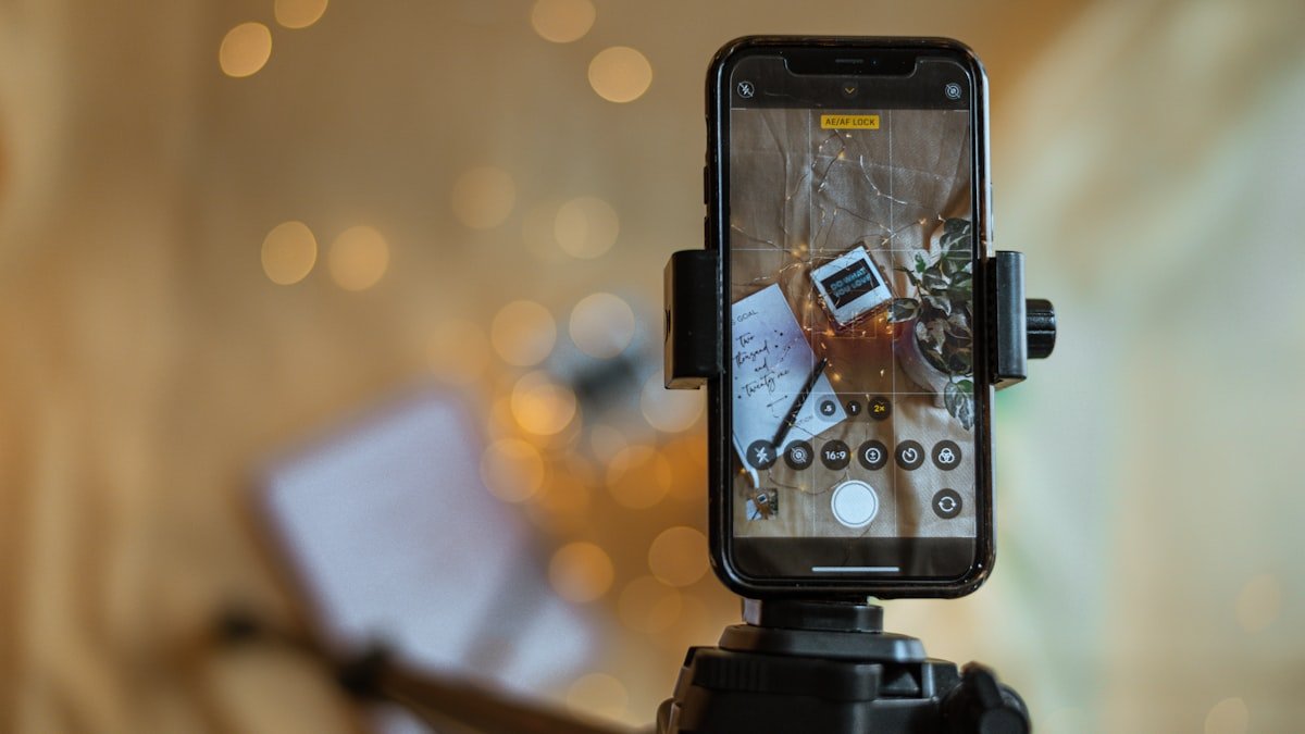 Celular em tripé gravando um vídeo ao lado de um caderno com roteiro para Reels escrito à mão